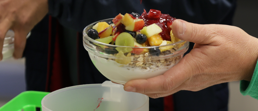 Eine Person gießt Fruchtsoße auf ihr Müsli mit Obst.