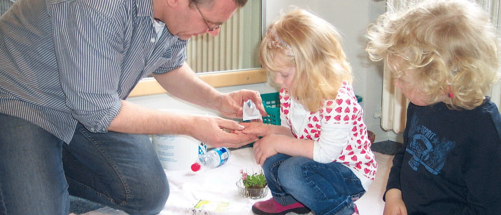 Einpflanzen Ein Mann schüttet zwei kleinen Kindern Pflanzensamen auf die Hand. Die Kinder pflanzen etwas ein.