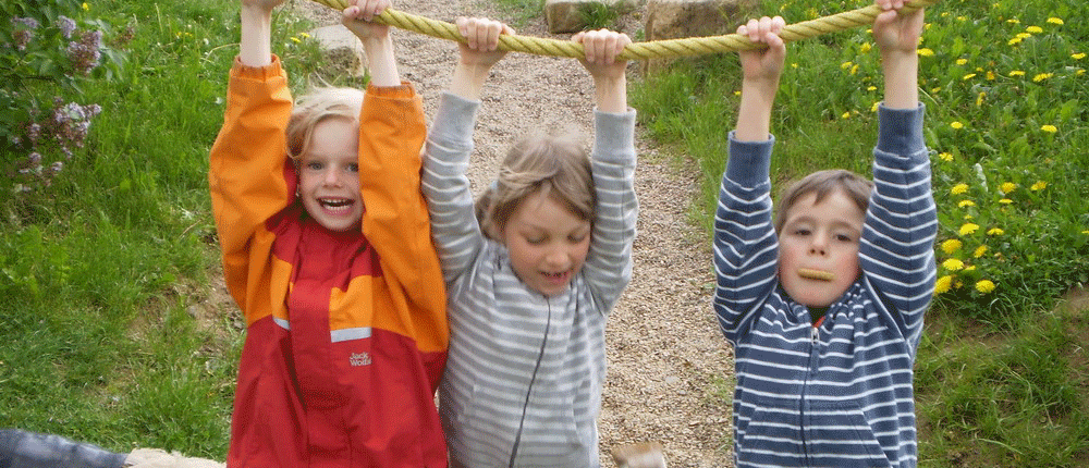 Spaß am Tau Drei Kinder hängen an einem hängenden Tau und haben Spaß.