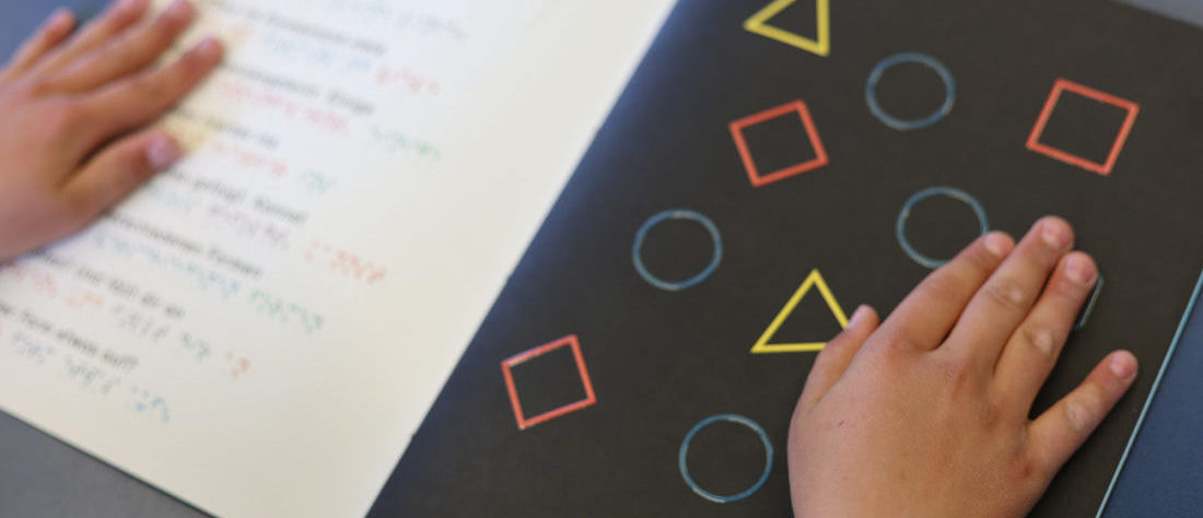 Ein Buch, das in Brailleschrift geschrieben ist. Kinderhände lesen darin.