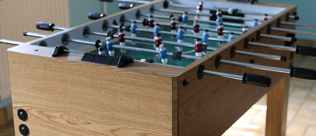 Ein Kicker steht in einem Raum, bereit für ein spannendes Spiel. Der Tisch ist mit den typischen Figuren und Stangen ausgestattet, die das Spiel ermöglichen.