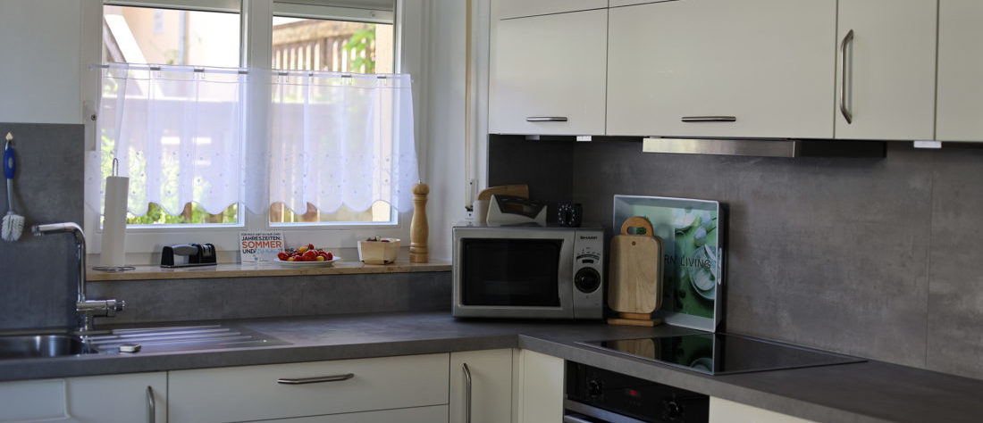 Ein Ausschnitt einer weißen, modernen Küche, in der eine Mikrowelle und Herd mit Backofen sichtbar ist. Die saubere, helle Umgebung vermittelt einen modernen und funktionalen Eindruck