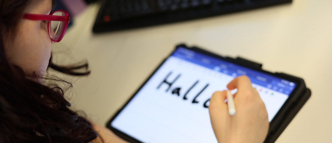Eine Schülerin schreibt das Wort „Hallo“ auf einem Tablet. Das Gerät wird genutzt, um Texte digital einzugeben, und zeigt eine moderne Form des Lernens und Arbeitens.