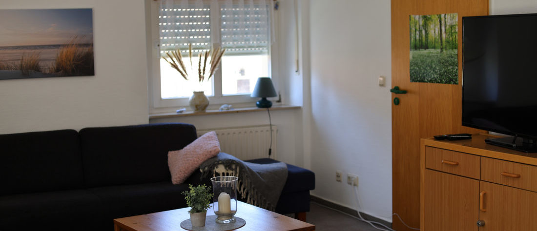 Ein Wohnzimmer mit einem Sofa und einem kleinen Tisch. An der Seite des Raumes befindet sich ein Fernseher.