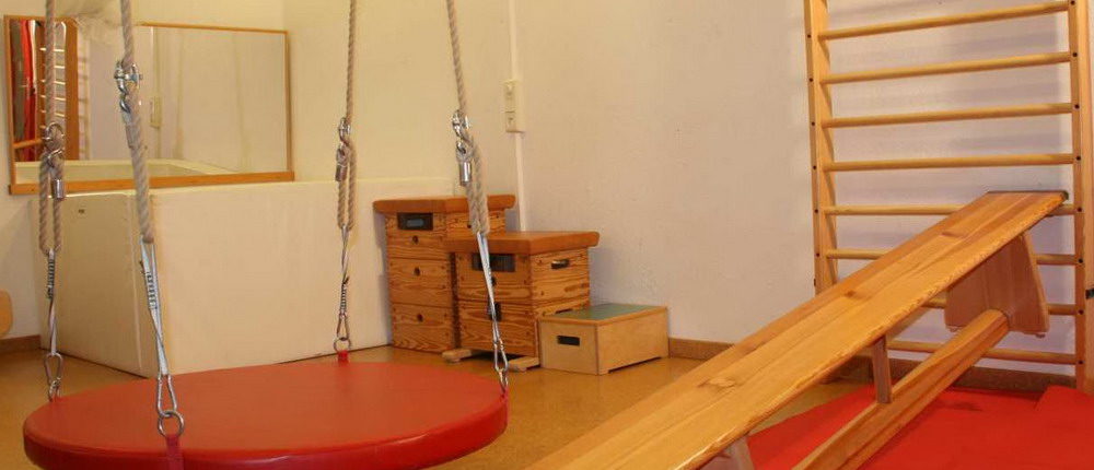 Bewegungsraum Ein Raum mit einer Schaukel, Sprungkästen und einer Sprossenwand. An der Wand hängt eine Sportbank.