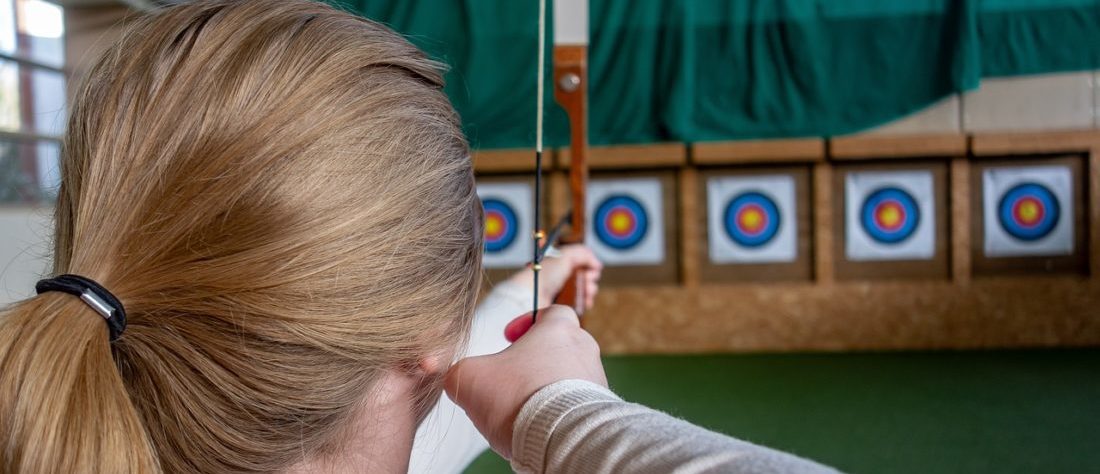 Ein Mädchen zielt mit einem Bogen auf Zielscheiben.