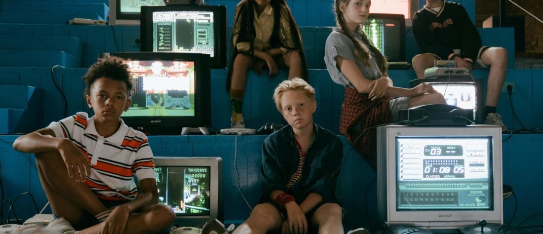 Eine Gruppe von Jugendlichen sitzt auf einer Treppe mit Monitoren und Computern. Sie wirken sehr cool.