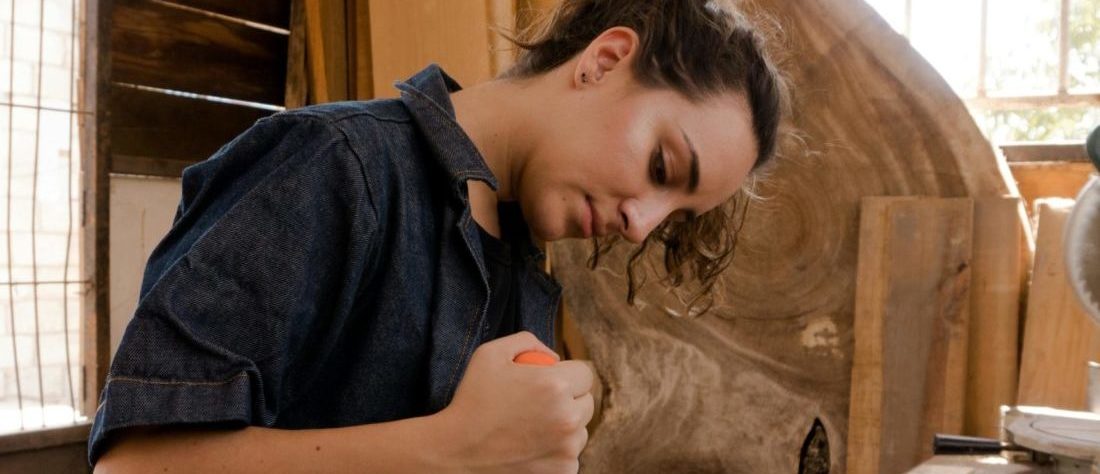 Ein Mädchen arbeitet mit einem Dremel an einem Holzstück.