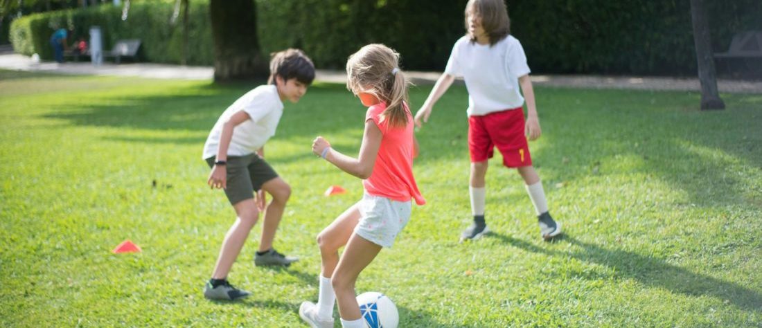 Drei Kinder spielen auf einem Rasen Fußball.