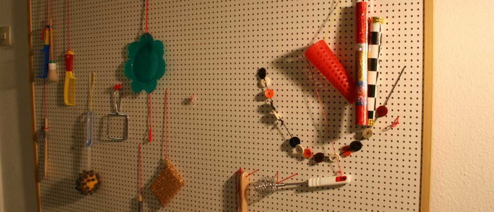 Tastwand Eine Wand mit vielen kleinen Löchern, in denen verschiedene Materialien zum Anfassen hängen.