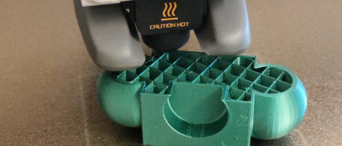 IMG_20250320_073045 Der Druckkopf des 3D-Druckers beim Drucken eines grün-metallischen Objektes.