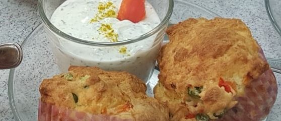 Frische Gemüsemuffins neben einem ecker Quark-Dip, in dem eine Karotte steckt.