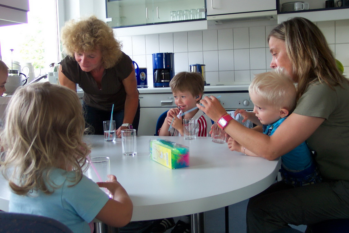 Kinder und Erwachsene trinken an einem Küchentisch.