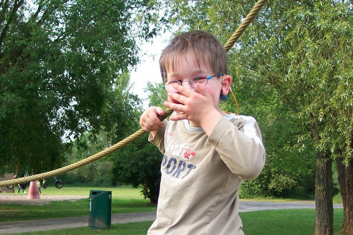 Ein Kind hält sich an einem Tau fest und lacht in die Kamera.