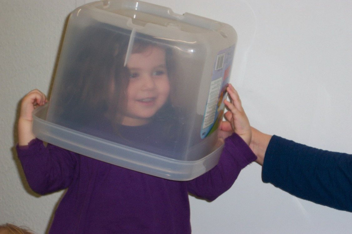 Ein Kind hat eine durchsichtige Kiste über dem Kopf und lacht.