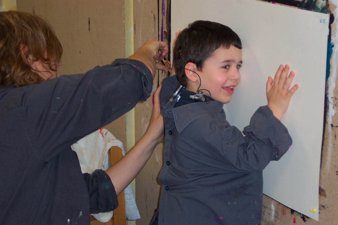 Ein Kind steht an einer weiße Plakatwand und lacht.