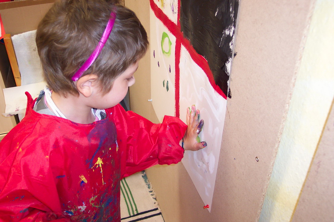 Ein Kind malt mit seiner Hand Fingerfarben an ein Plakat