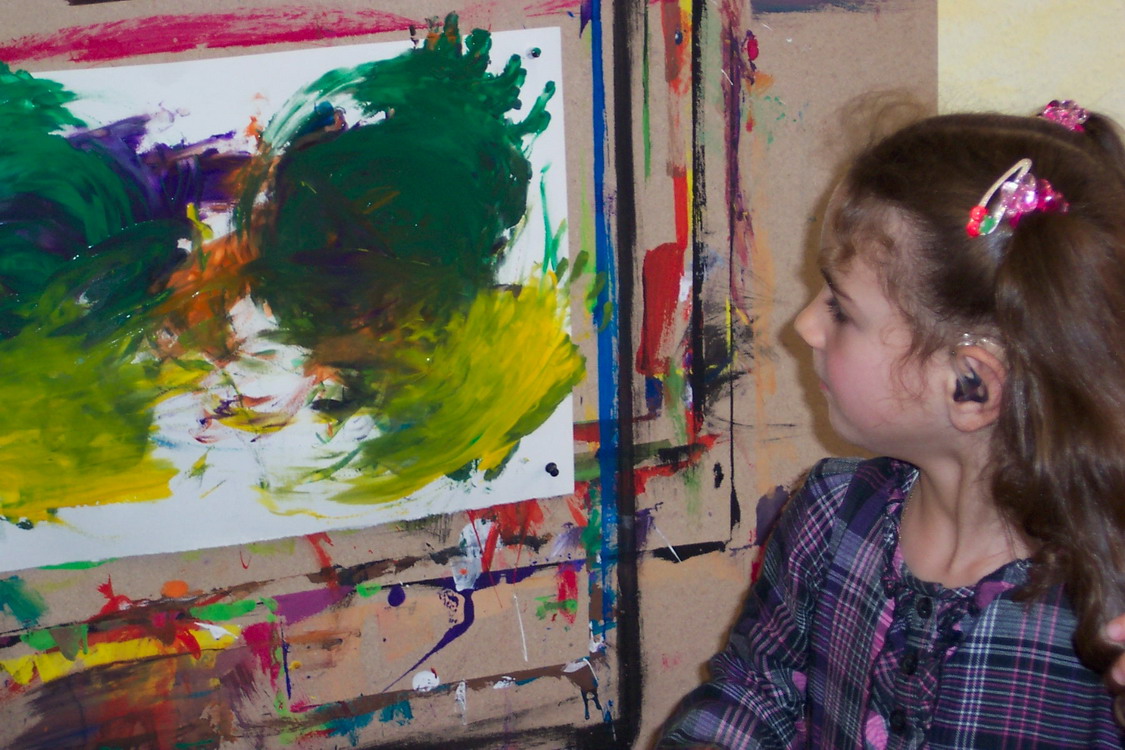 Ein Kind schaut sich sein gemaltes Kunstwerk an.