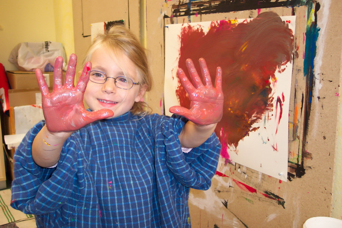 Ein Kind zeigt seine mit Fingerfarben eingefärbte Hände und freut sich.