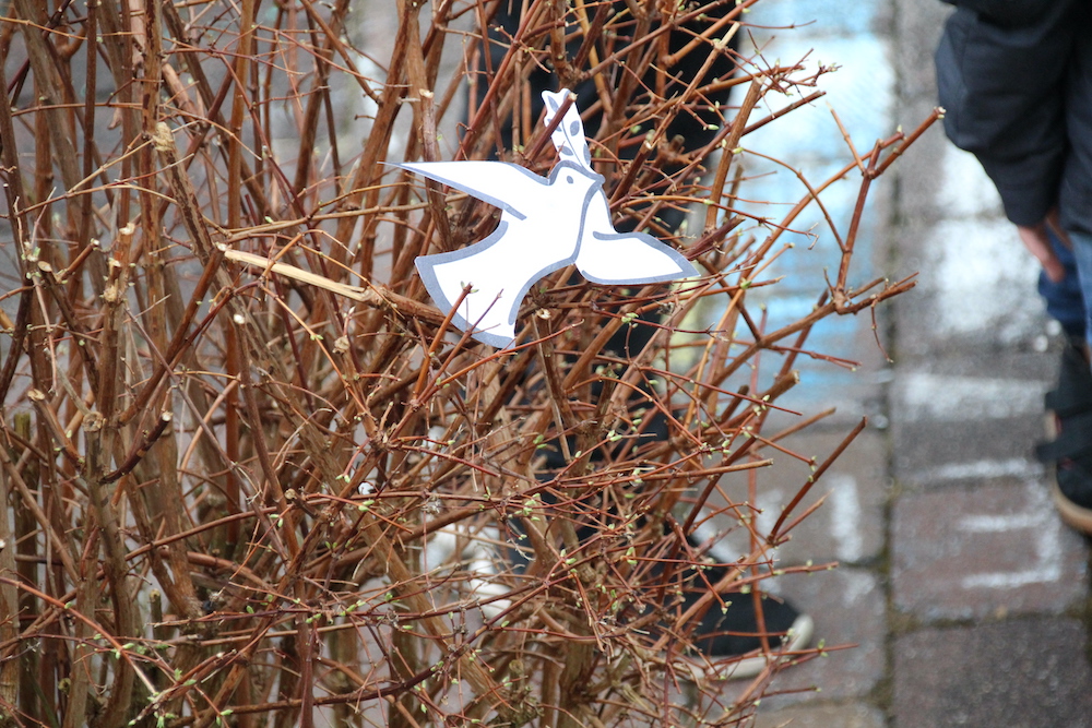 Eine Friedenstaube aus Papier liegt in einem Busch.