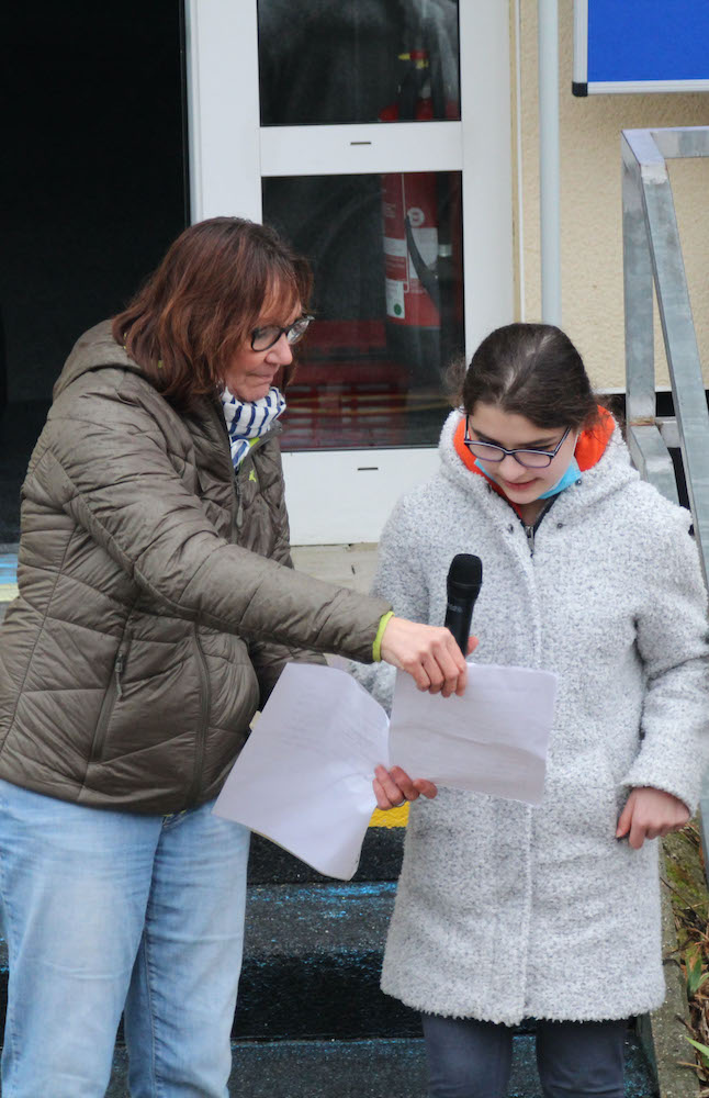 Eine Erwachsene Person und eine Schülerin lesen etwas vor.