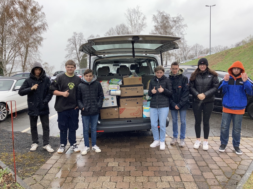 Schülerinnen und Schüler stehen vor einem vollgeladenem Bus.