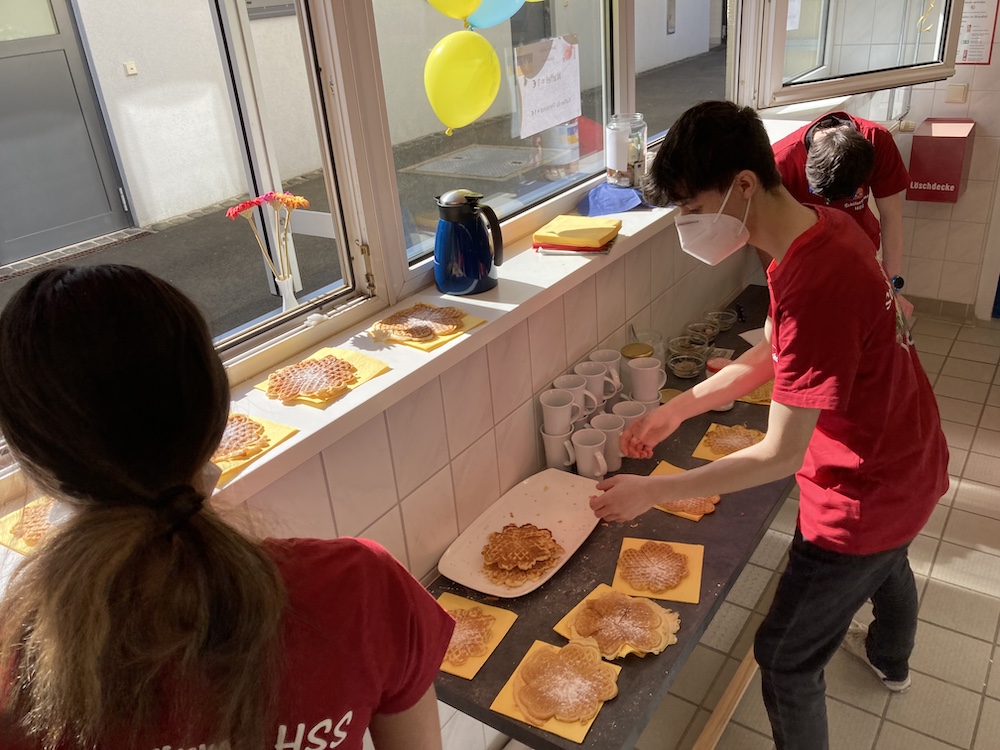 2 Schülerinnen und Schüler verkaufen an einem Fenster Waffeln.