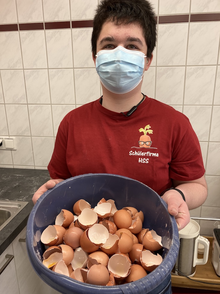 Ein Schüler zeigt eine große Schüssel mit Eierschalen.